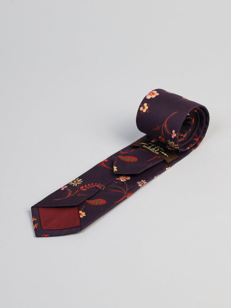 The Liberty of London Tana Lawn™ Swedish Tie by ID Menswear is handmade in Brooklyn from luxurious cotton, featuring a red floral and leaf design on light gray with a dark purple rolled-up finish.