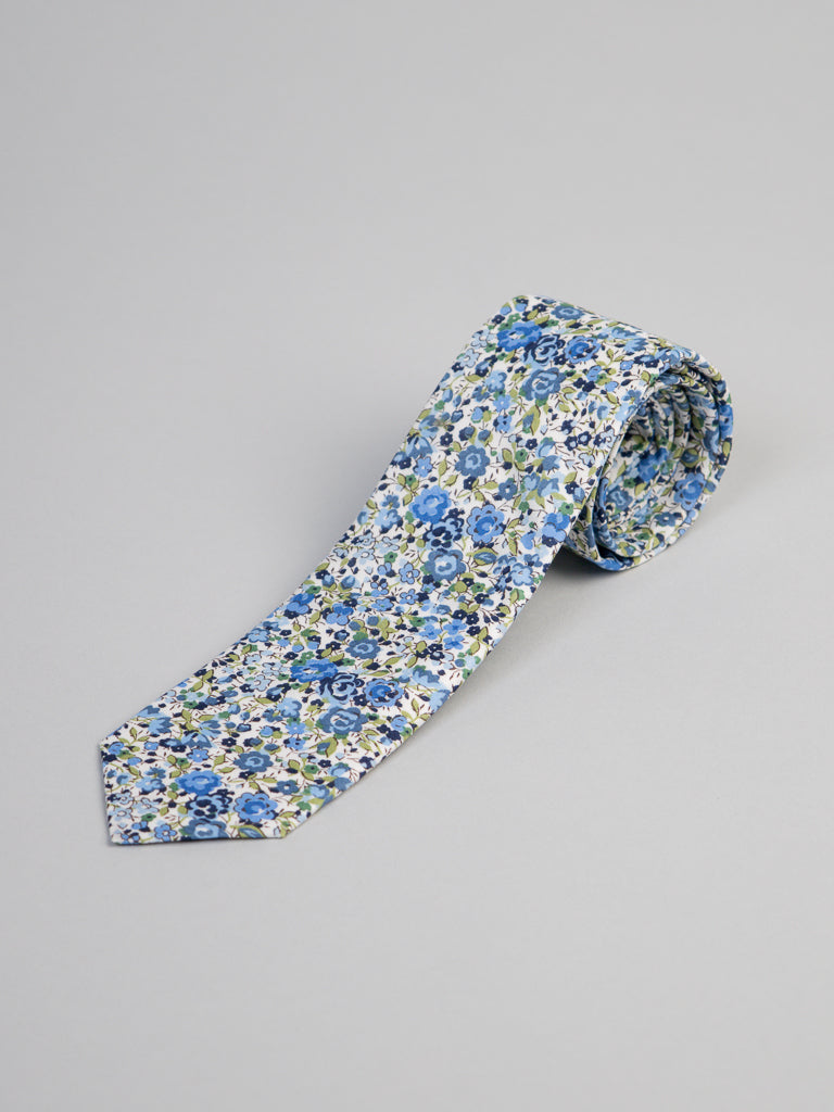 The ID Menswear Liberty of London Tana Lawn™ Emma Tie features a blue, green, and white floral pattern on luxurious cotton, shown rolled-up against a light gray background.