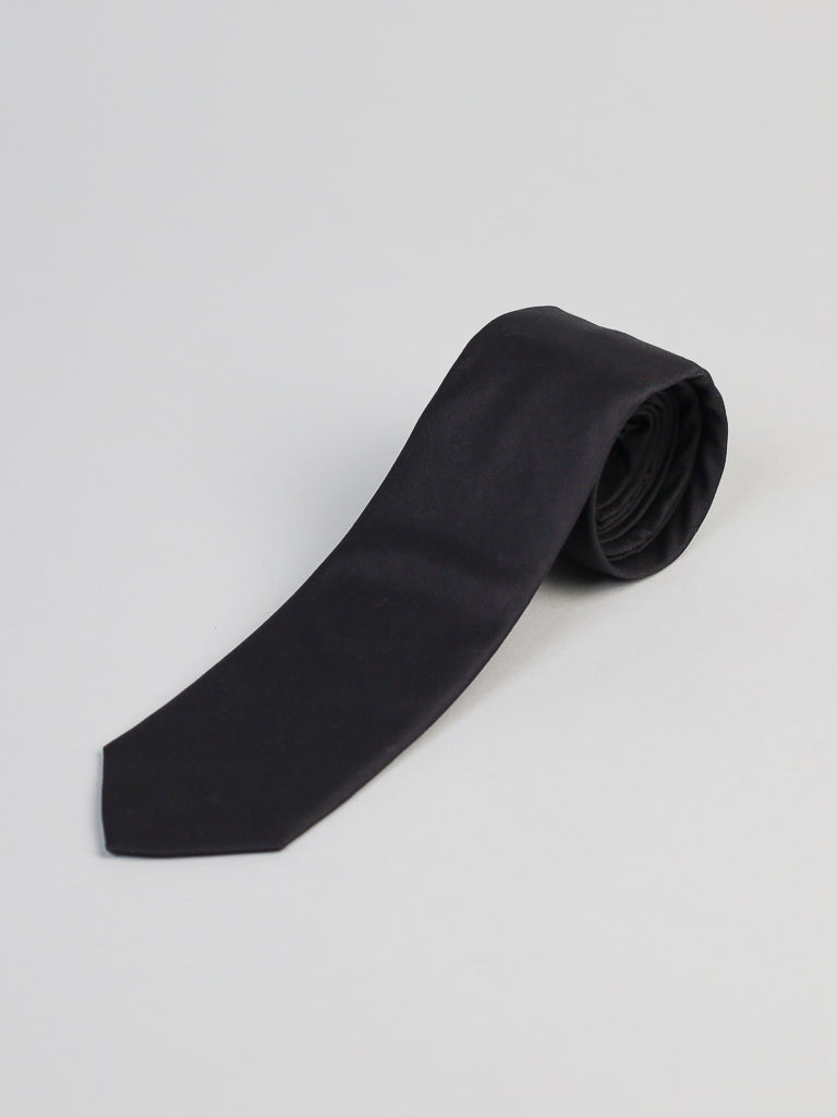 The New Black Cotton Tie by ID Menswear, handmade in Brooklyn, is shown neatly rolled on a plain light gray background.