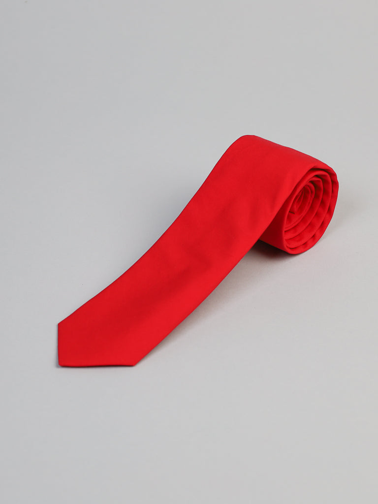 The Rouge Cotton Tie by ID Menswear, a bright red handmade piece, is rolled up and displayed on a light gray surface.
