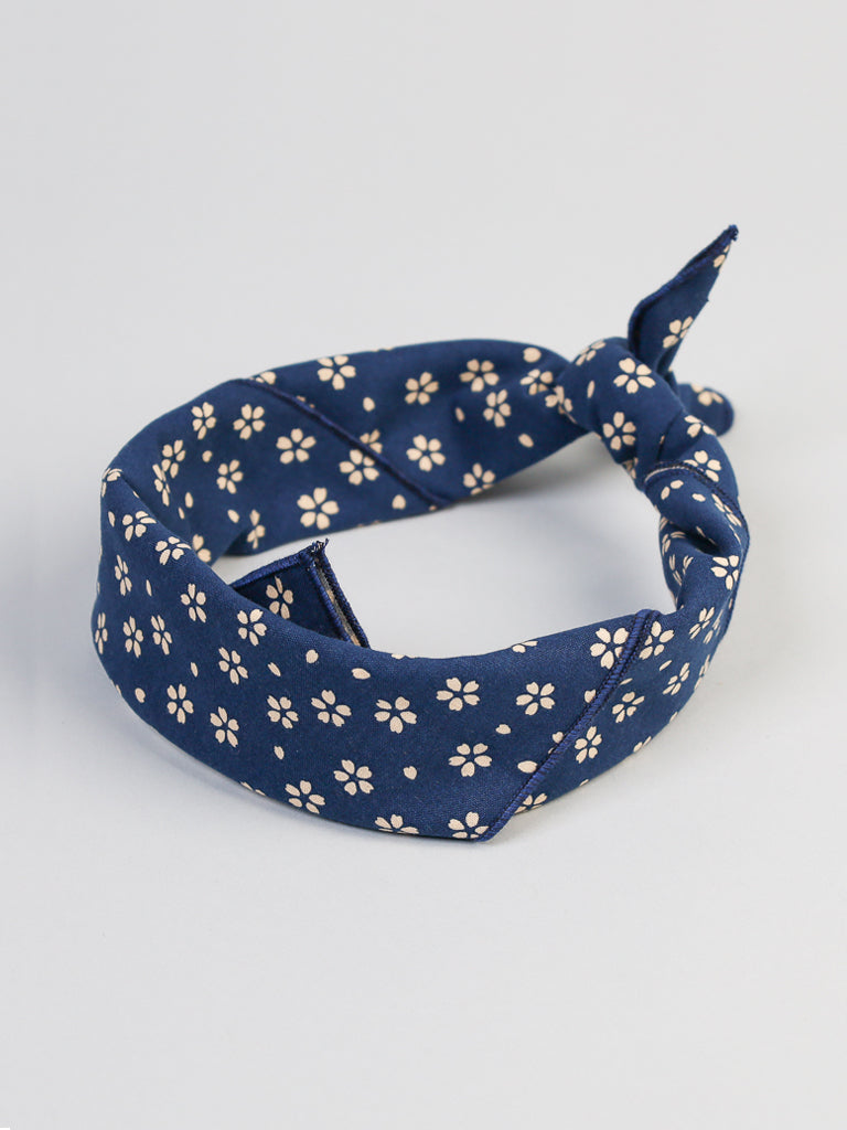 Introducing the Japanese Sakura Bandana by ID Menswear: a blue cotton headband with a white cherry blossom pattern. It features a stylish knot on one side and has a plain light gray background.