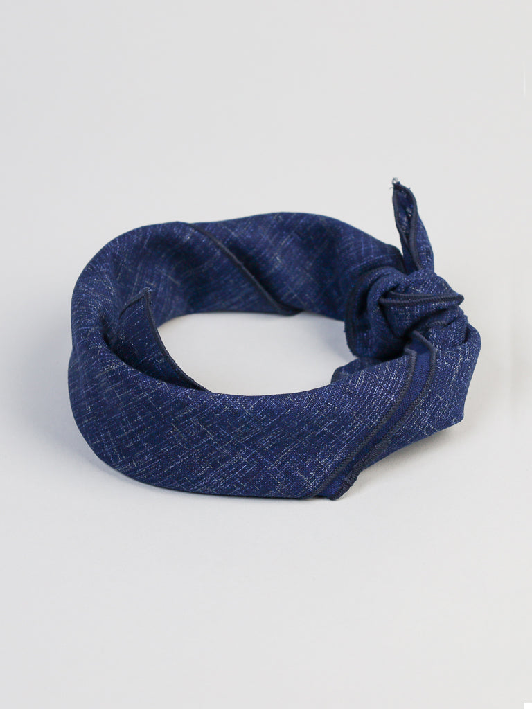 The Samurai Bandana from ID Menswear is showcased against an indigo background, featuring a blue neckerchief with a kasuri-like pattern tied neatly in a knot.