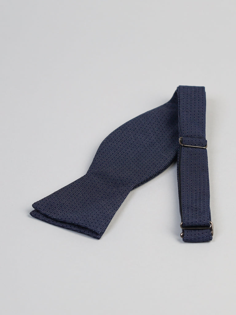 The Starry Night Cotton Bow Tie by ID Menswear is a navy blue, textured bow tie made from 100% cotton, handmade in Brooklyn with an adjustable strap, shown on a light gray background.