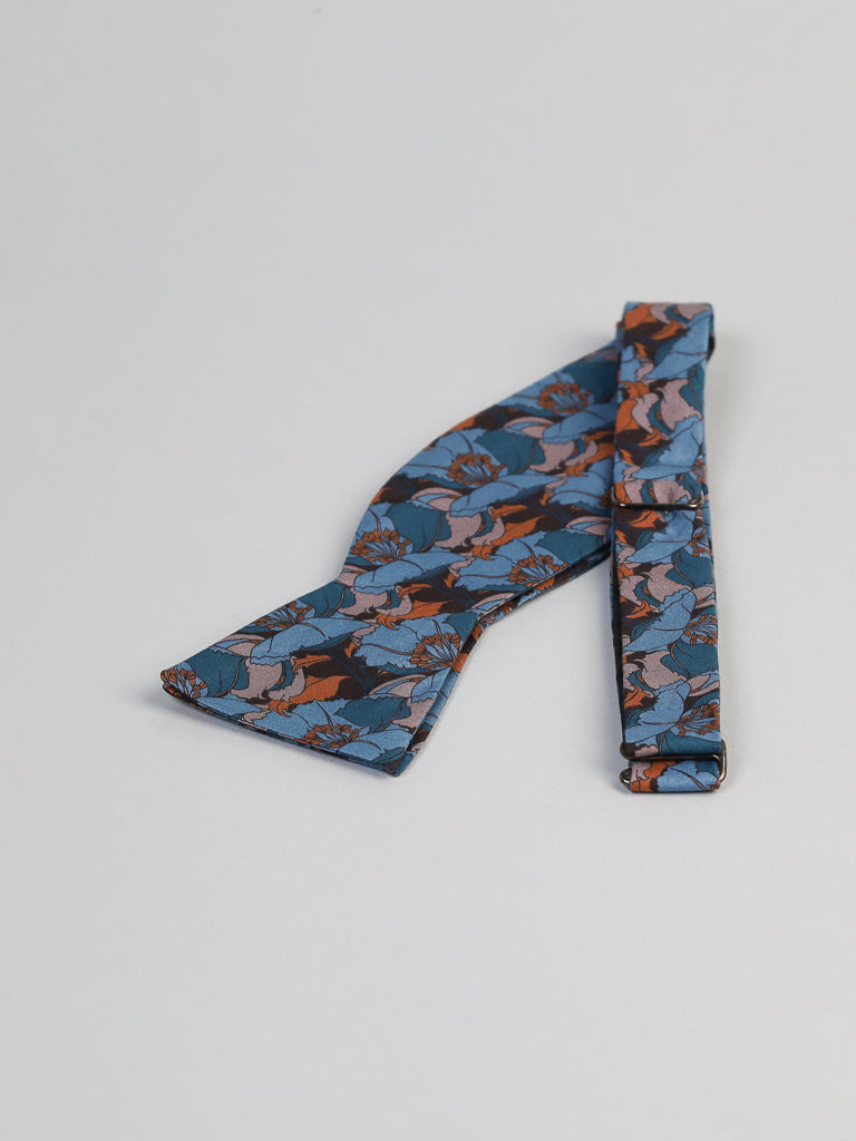 The ID Liberty of London Tana Lawn™ Eustacia Blue Cotton Bowtie from ID Menswear, known for its silk-like touch and crafted from floral patterned fabric, sits beside its matching folded strap. This handmade piece is made in Brooklyn and exudes artisanal charm.