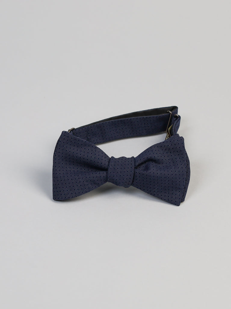 The Starry Night Cotton Bow Tie by ID Menswear is navy blue with a subtle textured pattern, handmade in Brooklyn. Displayed on a light gray background, this pre-tied cotton bow features an adjustable strap and secure clasp.