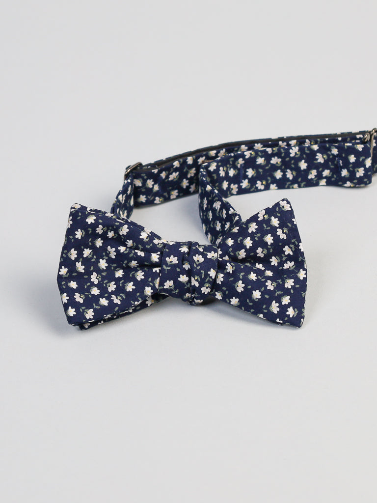 The Japanese Hana NW Printed Bow Tie by ID Menswear features a navy blue cotton fabric with small white floral prints, handmade in Brooklyn, and shown on an adjustable matching strap against a plain light background.