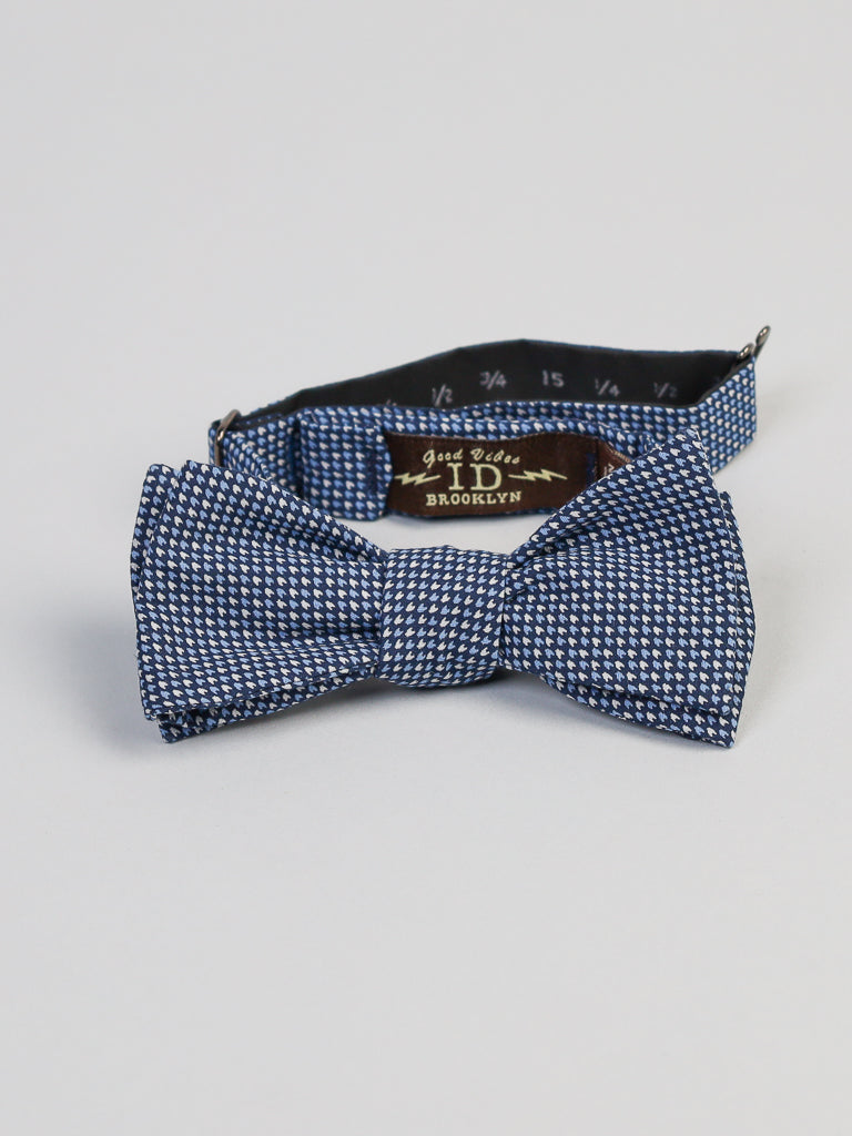 A blue and white patterned Japanese Ya Cotton Printed Bow Tie by ID Menswear, featuring a hint of Japanese print, rests on a light gray surface. The adjustable strap shows sizing details clearly, highlighting its sophisticated elegance. This piece is expertly handmade in Brooklyn.