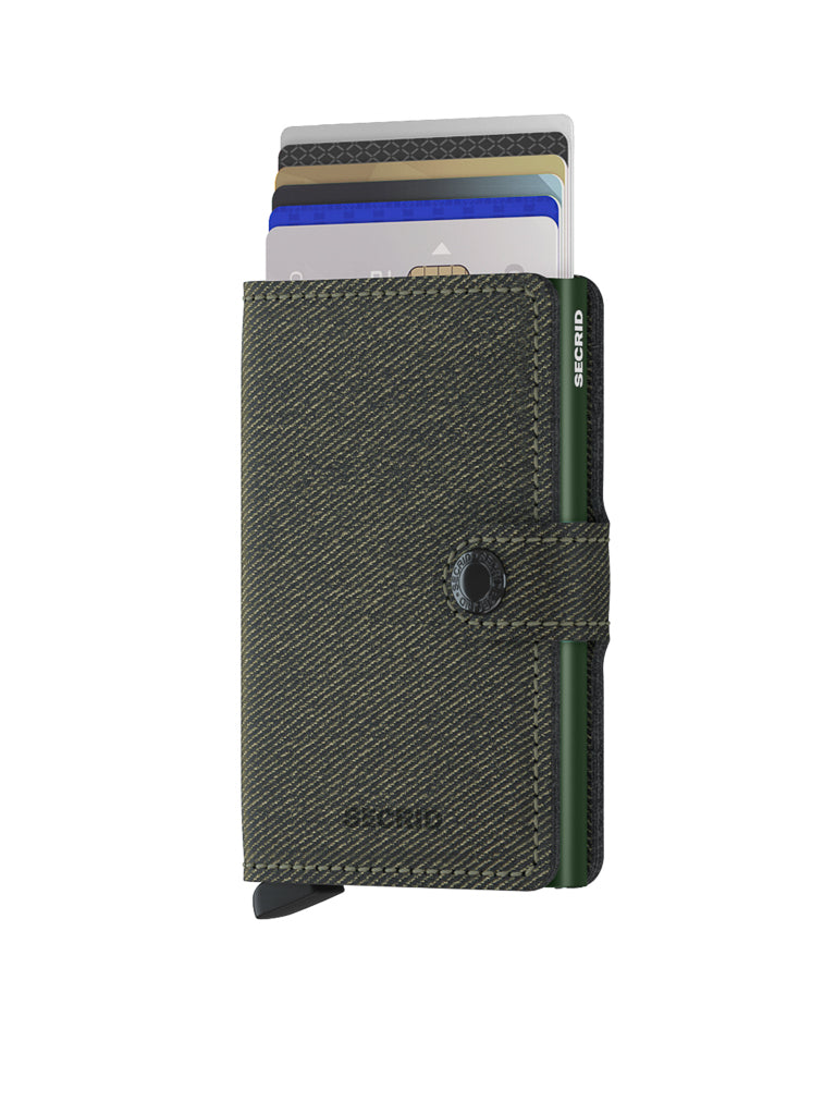 The Secrid Miniwallet Twist Twill Leather is a dark green, textured wallet with RFID protection, a button clasp, visible credit cards, and a card ejector lever at the bottom. This compact wallet stands upright against a white background.