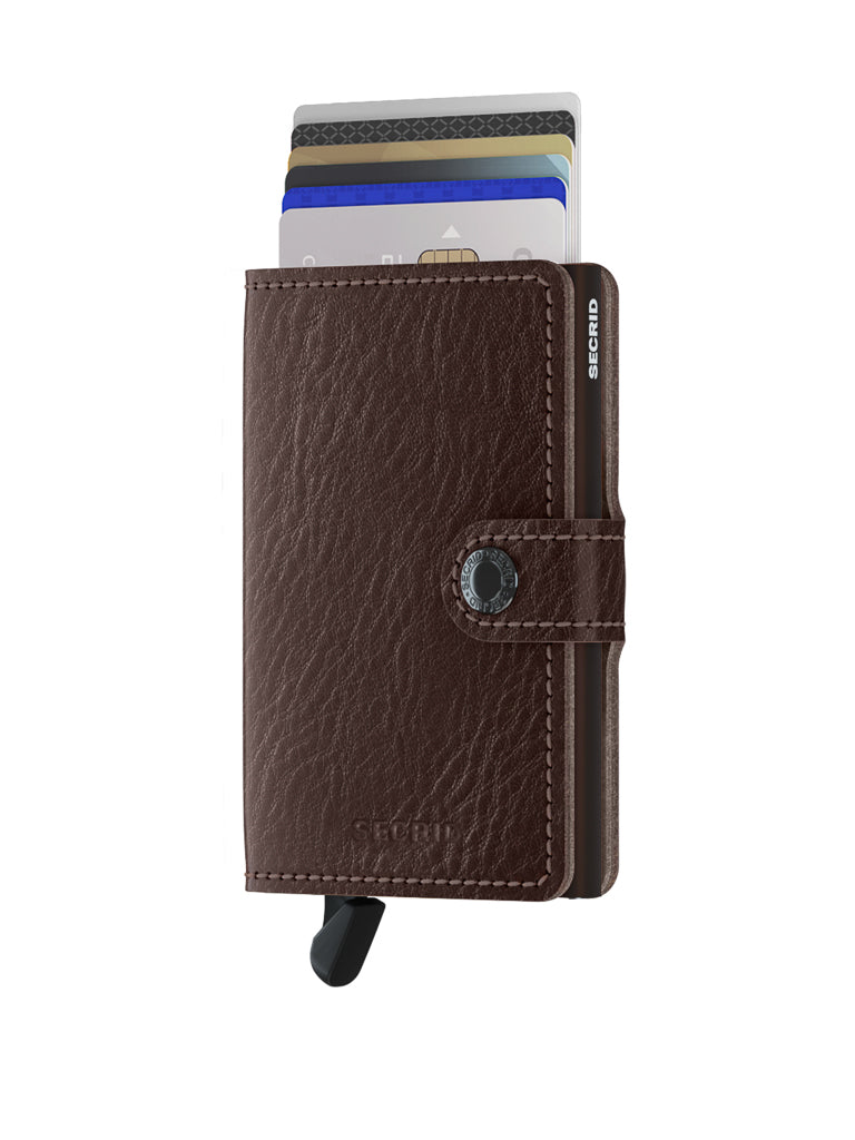 The Secrid Miniwallet Vegetable Tanned Leather in brown is shown on a white background. It features a snap closure, visible credit cards, and a black lever at the bottom for quick card access.