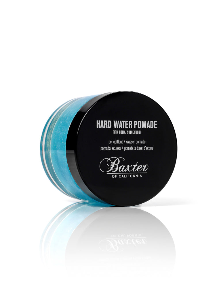 A jar of Baxter Hard Water Pomade Firm Hold and Shine Finish, featuring a black lid and blue gel, offers water-based styling for firm hold and shine, shown against a white background.