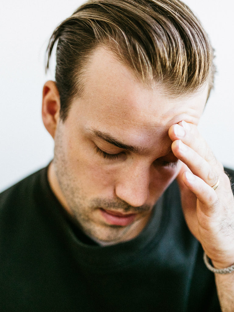A man with his hand on his forehead, his hair perfectly styled with Baxter Clay Pomade Firm Hold and Matte Finish.