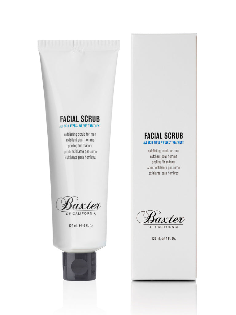 A tube and box of Baxter Exfoliating Facial Scrub to Tone and Smooth, both in white with black caps, display the product name in black and blue text and highlight its exfoliating formula for preventing ingrown hairs.