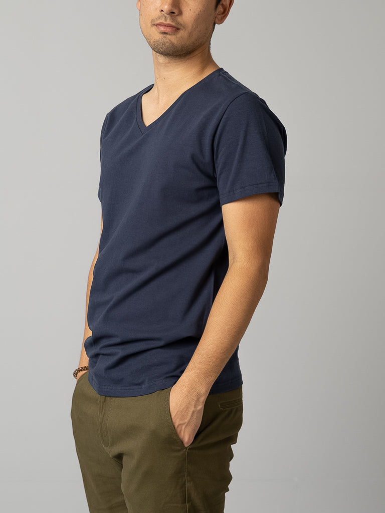 A person wearing the ID Menswear Form V Neck Tee in navy blue and olive green pants stands casually with hands in pockets against a plain light gray background, face unseen.