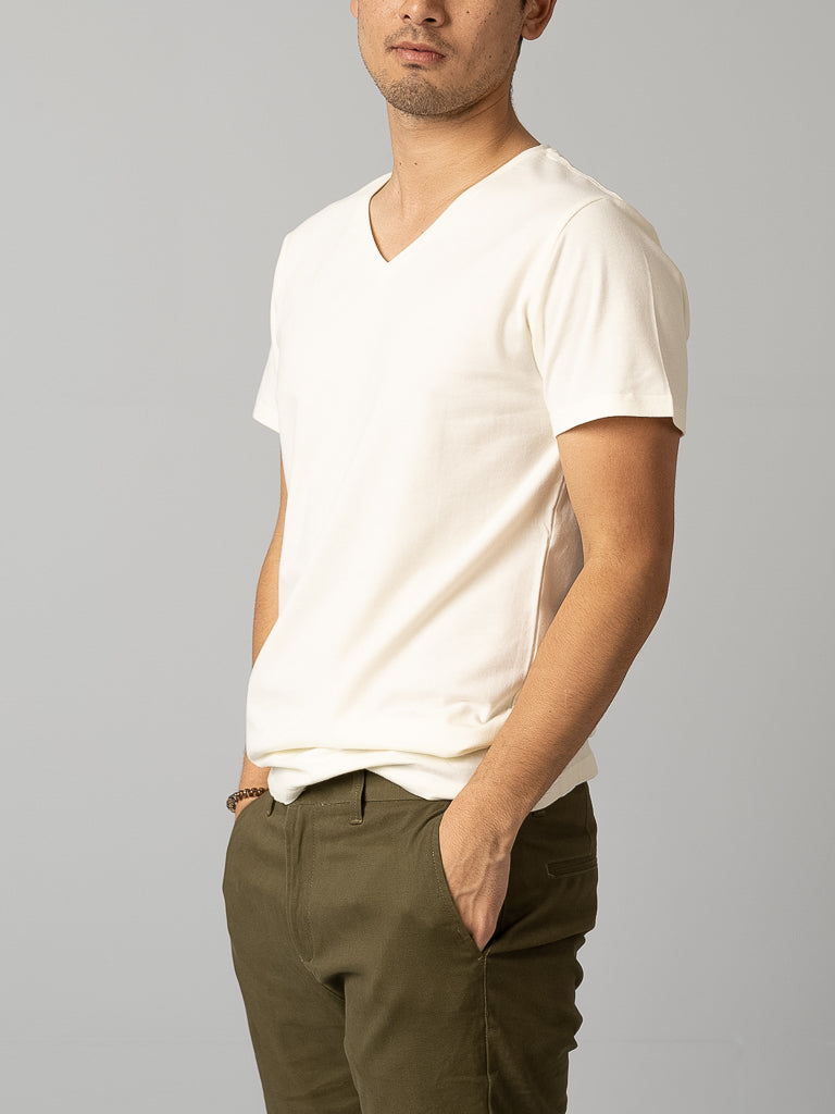 A person wearing an ID Menswear Form V Neck Tee and olive green pants stands against a neutral background with hands in pockets, adding a relaxed vibe perfect for any casual occasion. Their face is partially visible.