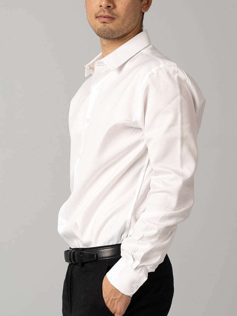 A man wears the ID Menswear Cotton Dress Shirt in slim fit, white, paired with black pants, standing sideways with one hand in his pocket against a plain gray background.
