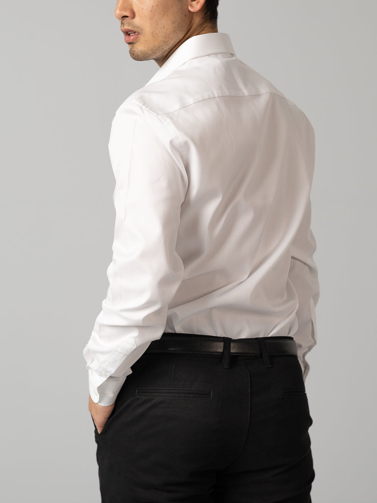 A man models the ID Menswear Cotton Dress Shirt in Slim Fit, shown from the back with one hand in his pocket, against a plain light gray background.