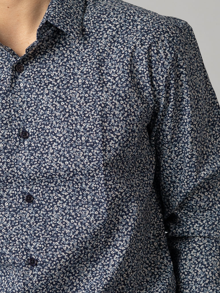 Close-up of a person wearing an ID Menswear navy blue, slim-fit ID Cotton Dress Shirt featuring a small white floral pattern. The long sleeves are buttoned, highlighting the textured fabric. The face is not visible in the image.