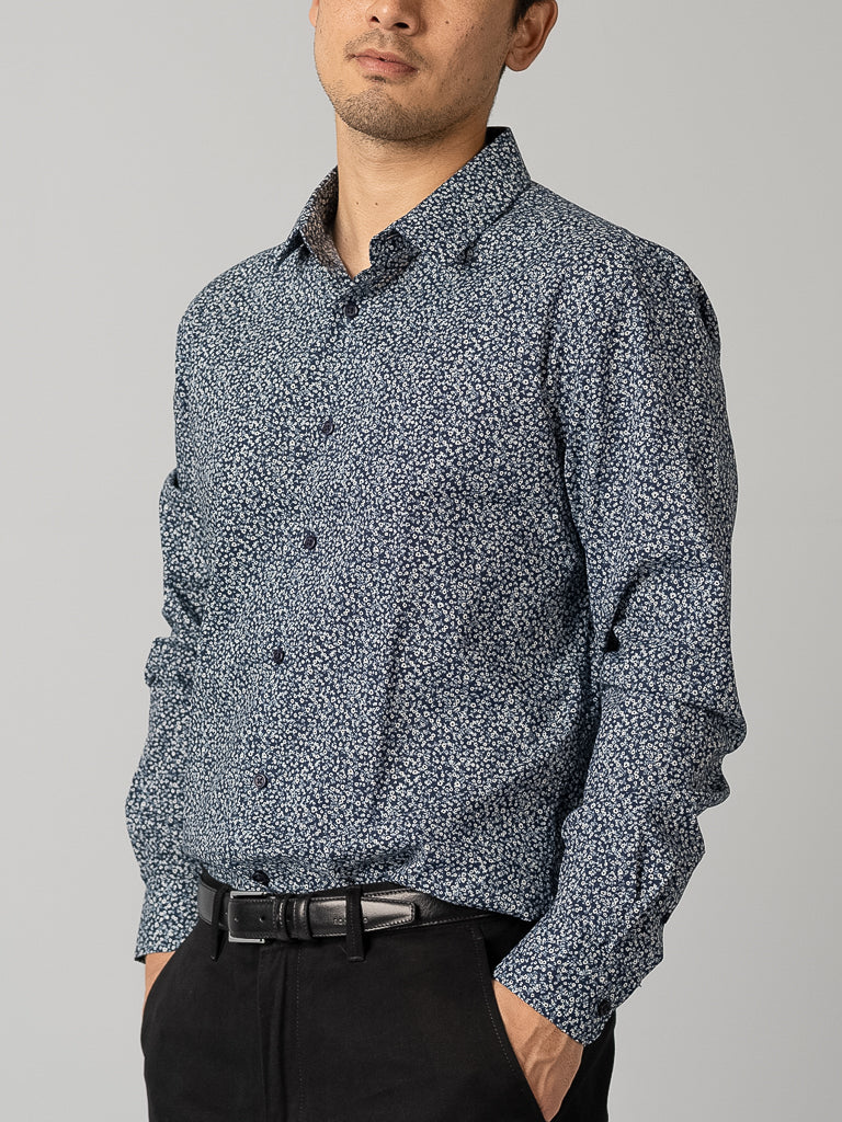 A man in an ID Menswear blue patterned ID Cotton Dress Shirt stands confidently against a gray background with his hands on his hips and a slight smile.