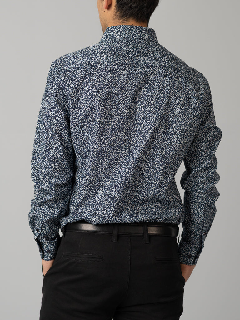 Wearing ID Menswears slim fit ID Cotton Dress Shirt with a blue floral pattern and neatly belted black pants, a person stands facing away from the camera against a plain gray background.