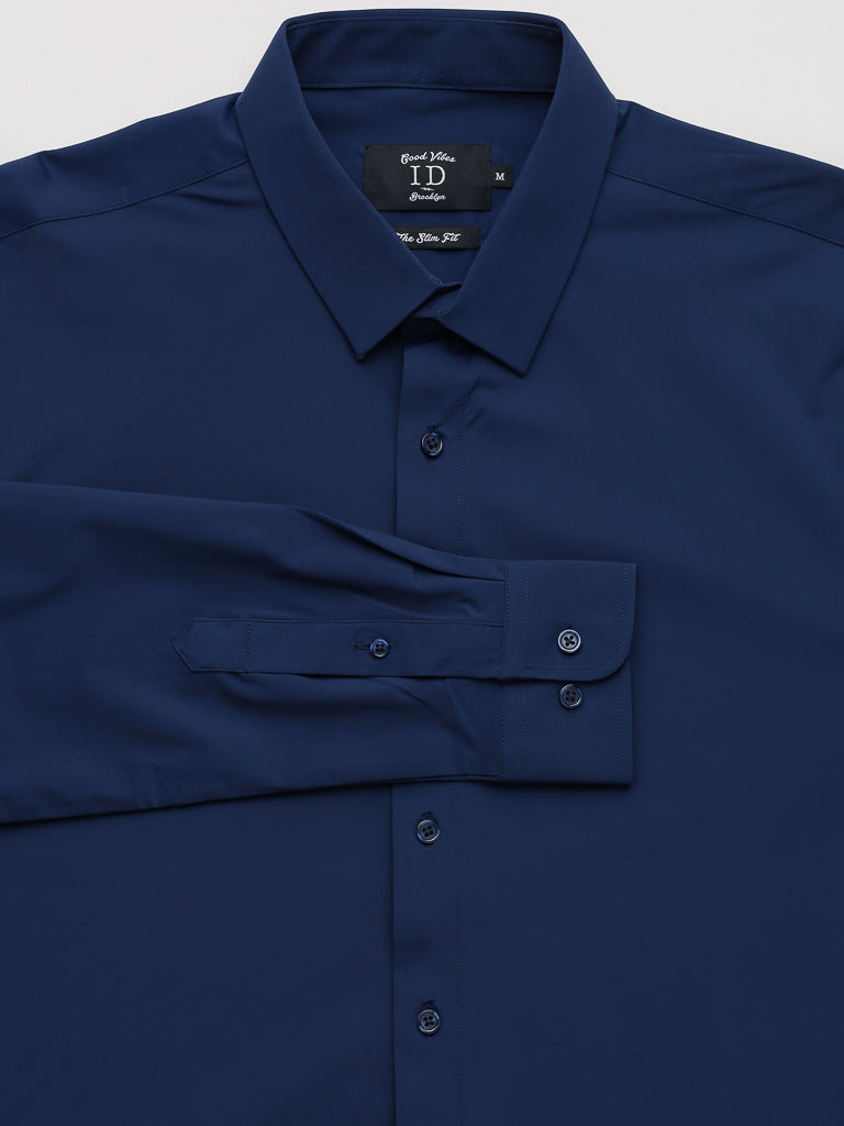 Displayed on a white background, the Axel 4-Way Stretch Dress Shirt from ID Menswear is a neatly folded, slim-fit dark blue shirt featuring a classic collar, buttoned cuffs, and front buttons. Made for comfort with its 4-way stretch design, a visible tag inside the collar shows size details.