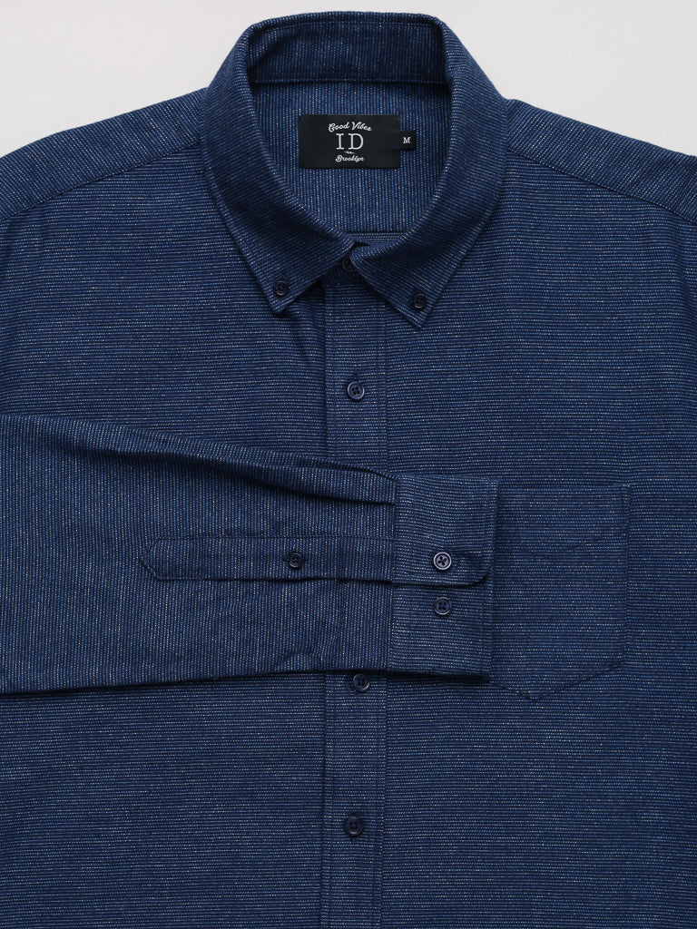 The Akira Cotton Button Down Shirt by ID Menswear is a regular-fit, blue, long-sleeve cotton shirt with a subtle textured pattern. It includes a front pocket and a black label inside the collar for size info. The sleeves are partially buttoned.