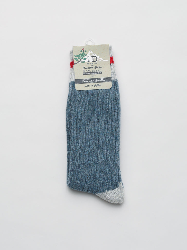The ID Menswear Wool Blend Socks feature a single blue ribbed sock with a gray toe and cuff. Ideal for cold weather, it includes a beige tag with green text and a top hanger, displayed against a white background.