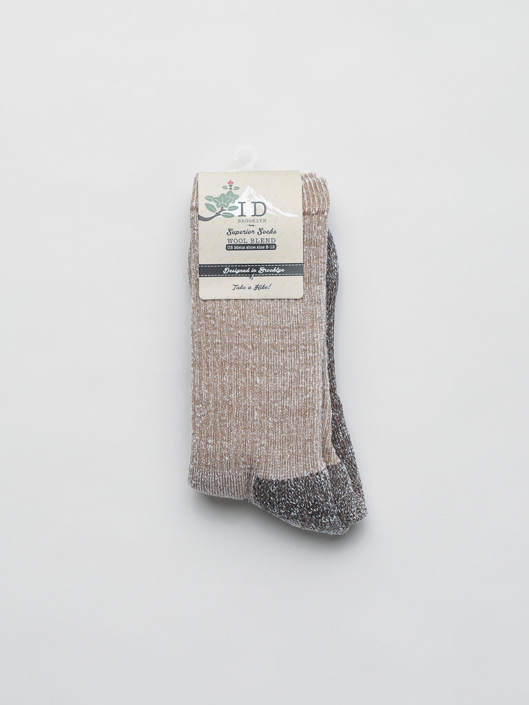 A pair of folded Merino Wool Blend Socks from ID Menswear, in beige and gray with a ribbed texture, provides cold-weather comfort. A cardboard label featuring text and leaf graphics set on a plain, light gray background is attached.