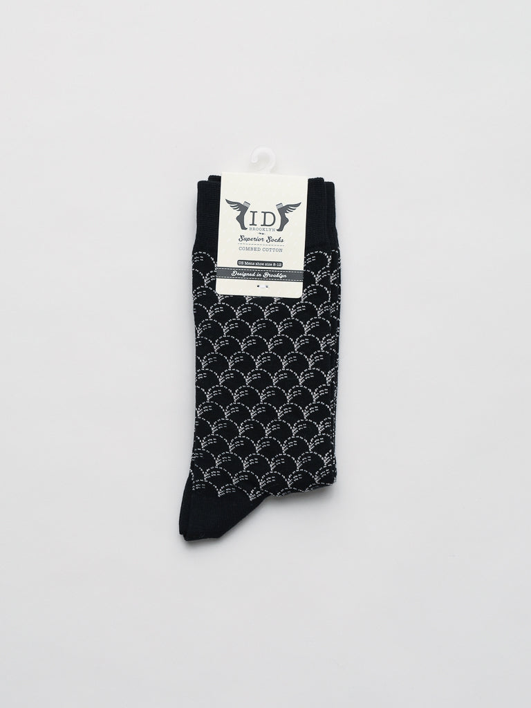 A pair of ID Menswears black Broken Waves Graphic Socks, featuring a white geometric arch pattern, displayed vertically on a plain white background. A label near the top promises premium comfort with a breathable, stretchy fit.