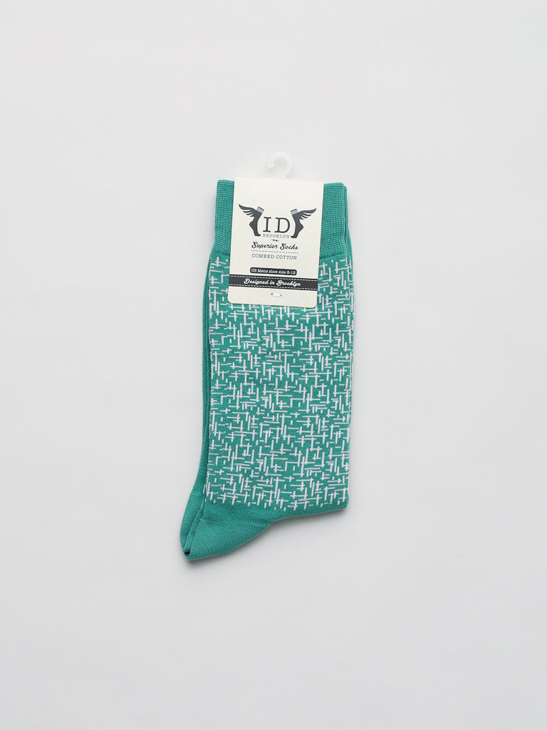 A pair of ID Menswear Urban Graphic Socks in green boast a white geometric pattern on a light gray backdrop. Crafted from soft combed cotton, they feature a paper label with the brand logo, accentuating their contemporary design.