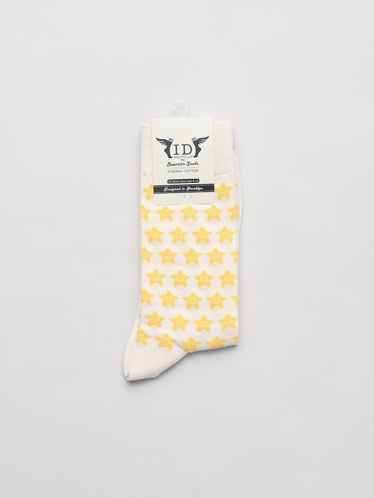 Twinkle Graphic Socks by ID Menswear: Cream-colored with yellow stars, attached to a logo-printed cardboard label. These fun gift socks are set against a white background, perfect for adding charm to any wardrobe.