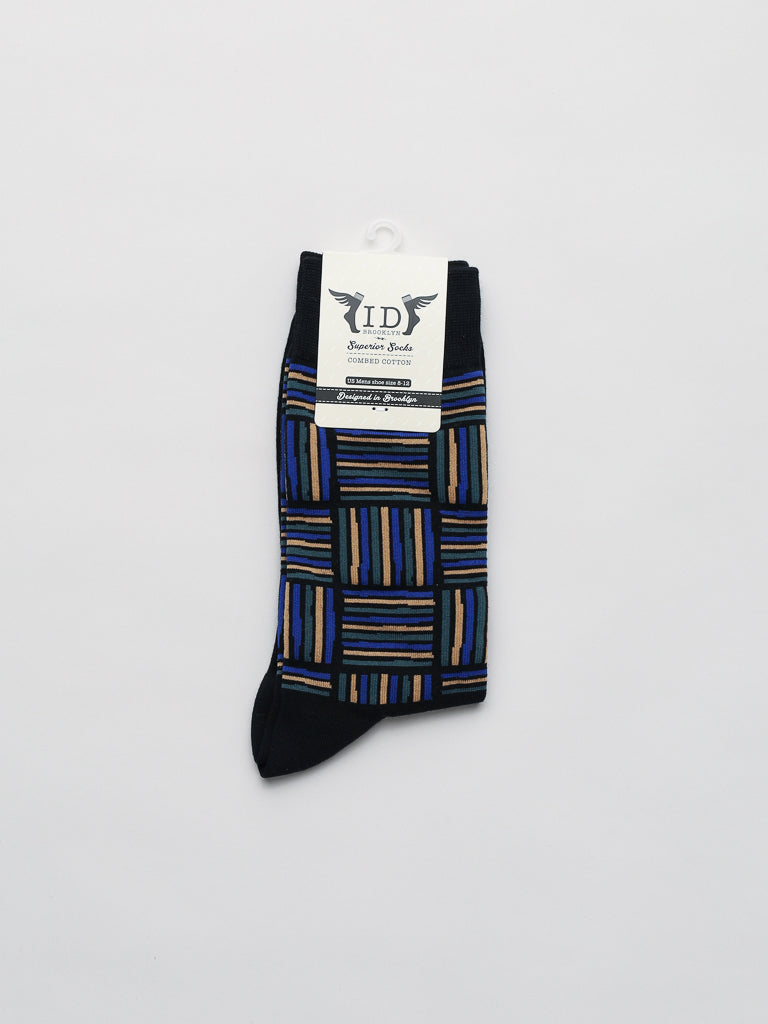A pair of Spongee Graphic Socks from ID Menswear, featuring black fabric with blue, brown, and purple geometric lines. Made from premium combed cotton for superior comfort, theyre folded neatly and secured with a branded tag displaying the logo and text on a white background with a top hook.