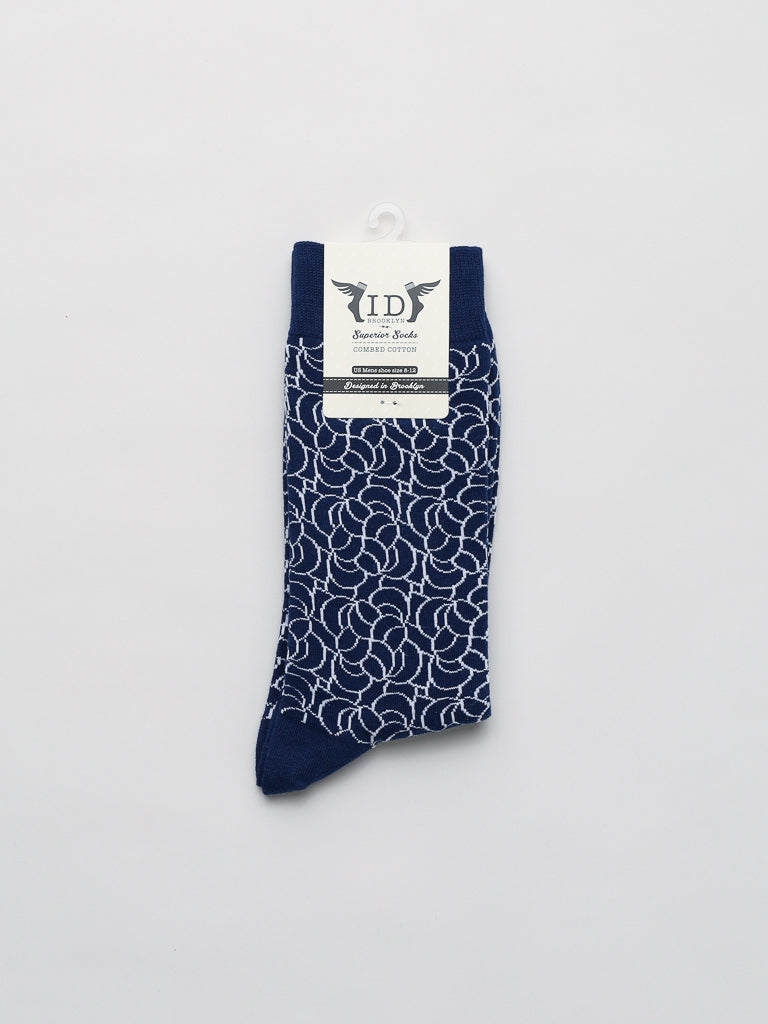 The Ellipsis Graphic Socks by ID Menswear are displayed flat against a white background. This single navy sock with intricate white floral patterns is made from combed cotton and features a white label with text and logo, ensuring comfort in mens breathable socks.