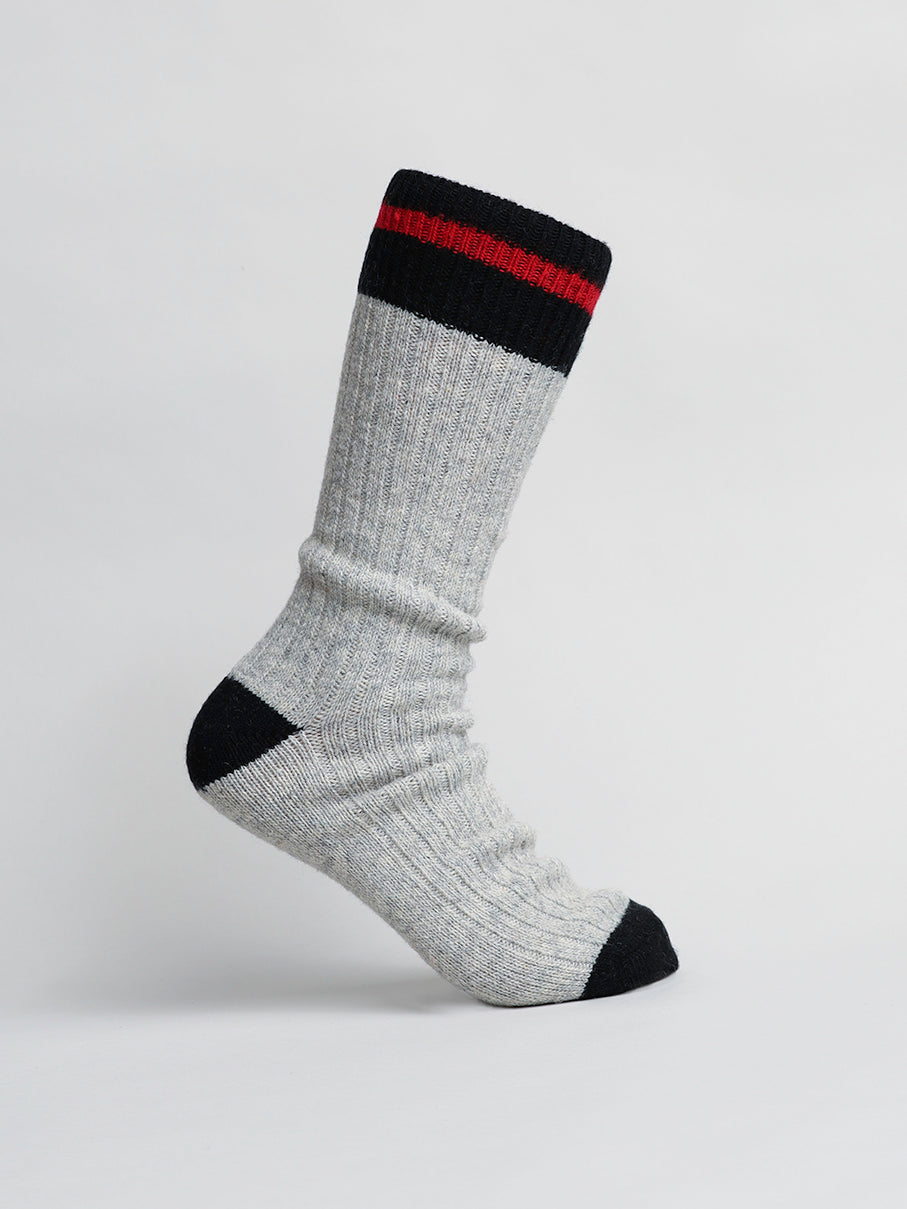 A single gray Wool Blend Sock by ID Menswear, featuring a ribbed texture with a black heel, toe, top band, and red stripe. Perfect for winter activities, the sock is displayed upright on a neutral background.