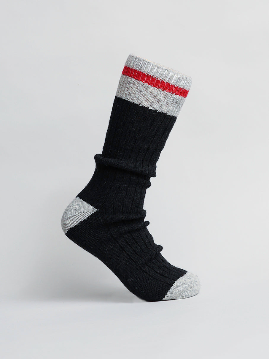 The black Wool Blend Sock by ID Menswear, designed for cold weather, has a ribbed texture, gray toe and heel, and a gray cuff with a red stripe. It is shown against a plain white background.