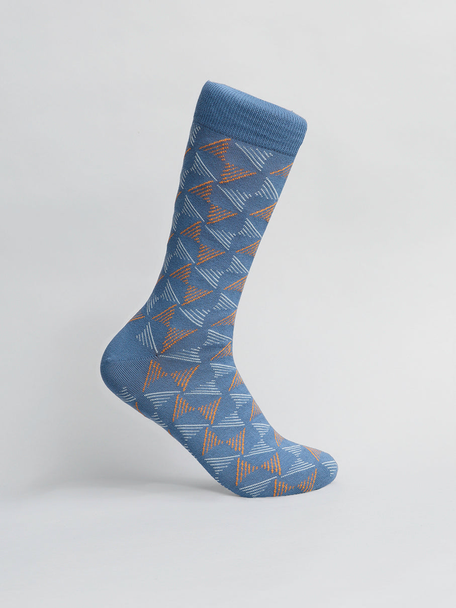 The Dreamlines Graphic Sock by ID Menswear is a comfy, single blue sock made from combed cotton. It features orange and white geometric triangles on a light background, highlighting its stylish design and breathability when positioned upright.