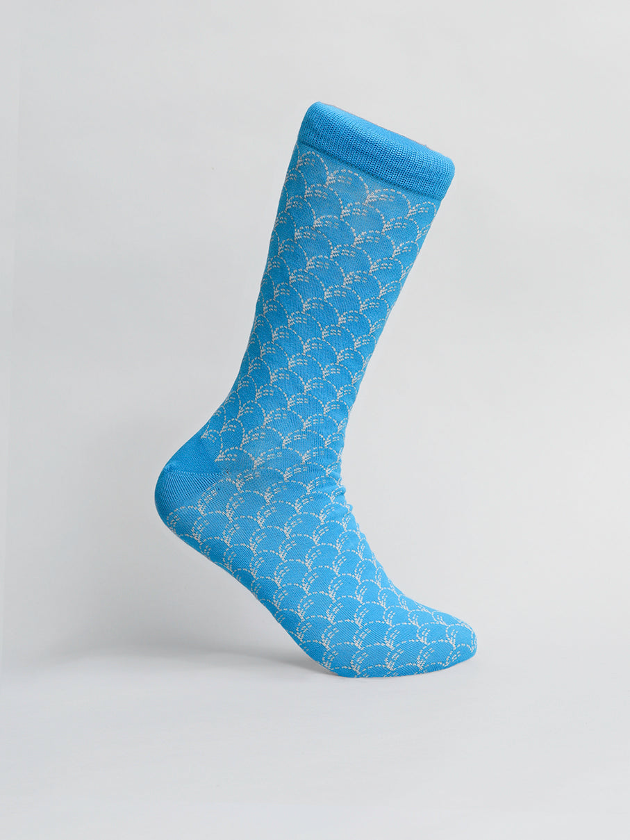 A single Broken Waves Graphic Sock by ID Menswear, made from breathable combed cotton with a light gray scallop pattern on blue. The stretchy sock is shown elevated against a plain background with the toe downward and cuff at the top for premium comfort.