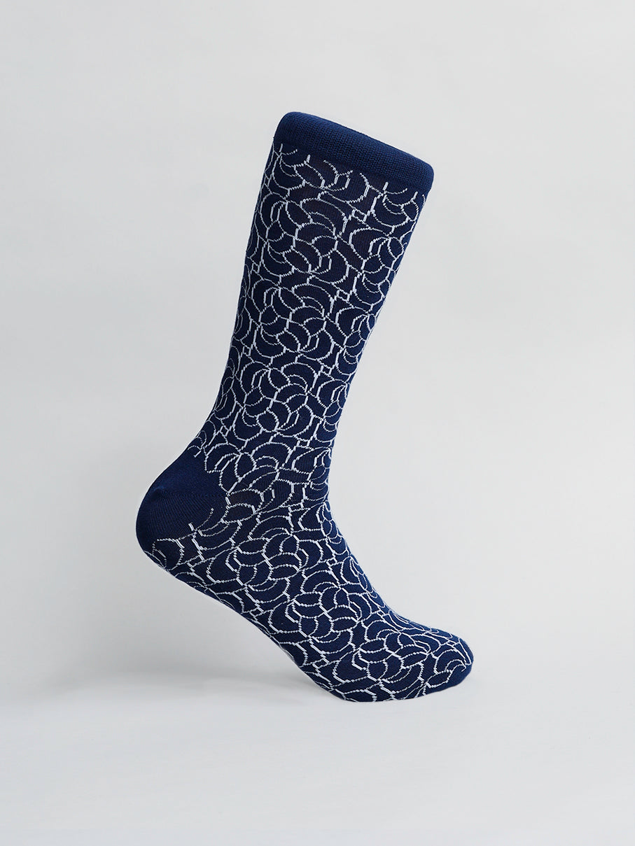 A single Ellipsis Graphic Sock by ID Menswear, in navy blue combed cotton with a white abstract pattern resembling floral or circular designs, is shown on a light gray background. The mens sock, known for breathable comfort, stands upright and angled right.