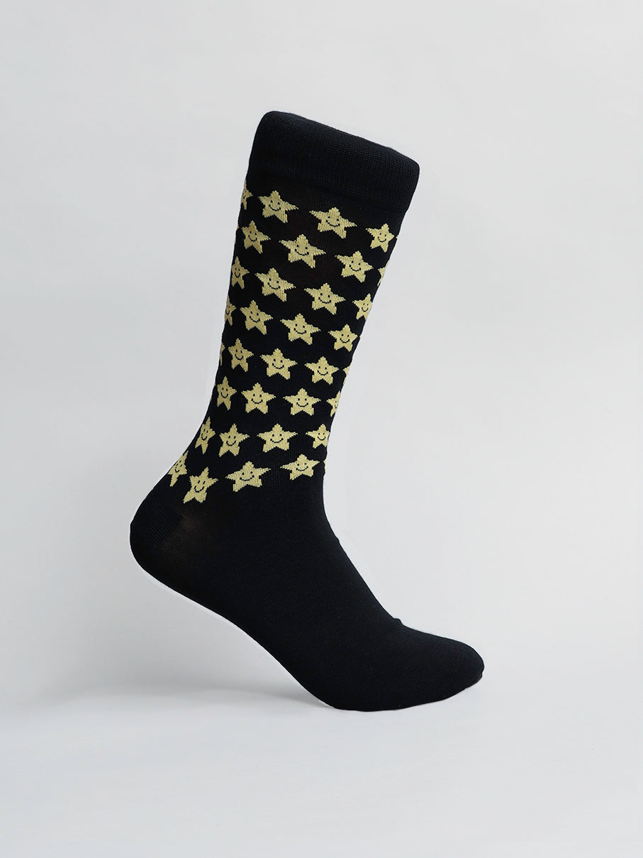 The ID Menswear Twinkle Graphic Socks feature a black design with yellow star patterns on a light background. Highlighted at an angle, these socks make a fun gift, combining style and comfort with quality combed cotton.