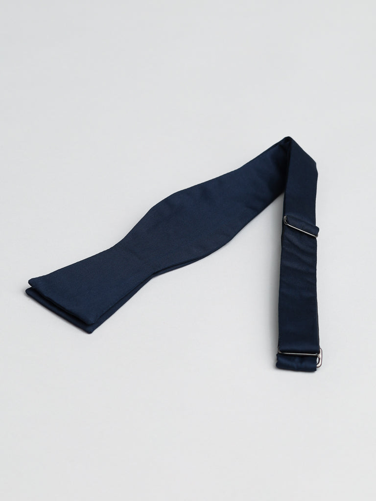 The Midnight Cotton Bow Tie by ID Menswear is a navy blue, untied cotton bow tie with adjustable metal hardware, handmade in Brooklyn—ideal for semi-formal occasions.