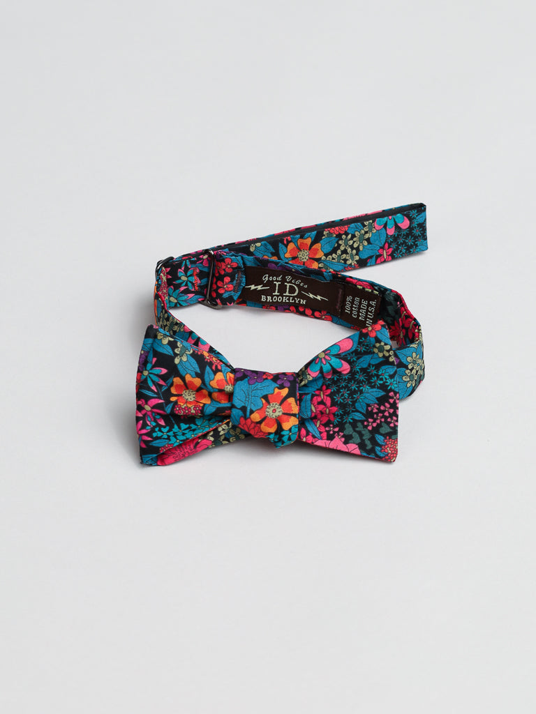 The ID Liberty of London Tana Lawn™ Ciara Cotton Bowtie by ID Menswear features a vibrant floral pattern in pink, orange, blue, and green on a dark backdrop, displayed on a light surface.