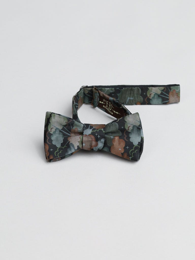 A vibrant Liberty of London Tana Lawn™ Cloud Nine cotton bow tie from ID Menswear features a green, brown, and white floral pattern against a plain white backdrop. The adjustable strap adds charm reminiscent of Libertys renowned designs.