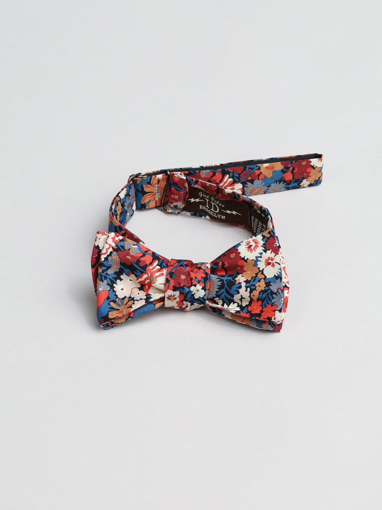 The ID Liberty of London Tana Lawn™ Kanazawa cotton bow tie by ID Menswear is handmade in Brooklyn, showcasing red, blue, and white floral patterns on an adjustable strap laid flat on a neutral background.