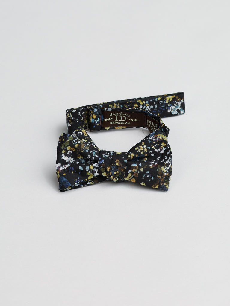 The ID Liberty of London Tana Lawn™ Reflection Cotton Bowties by ID Menswear is an elegant, handmade black bow tie with a floral pattern in blue, white, and yellow on white. This stylish accessory is crafted from Liberty of Londons renowned cotton and made in Brooklyn.