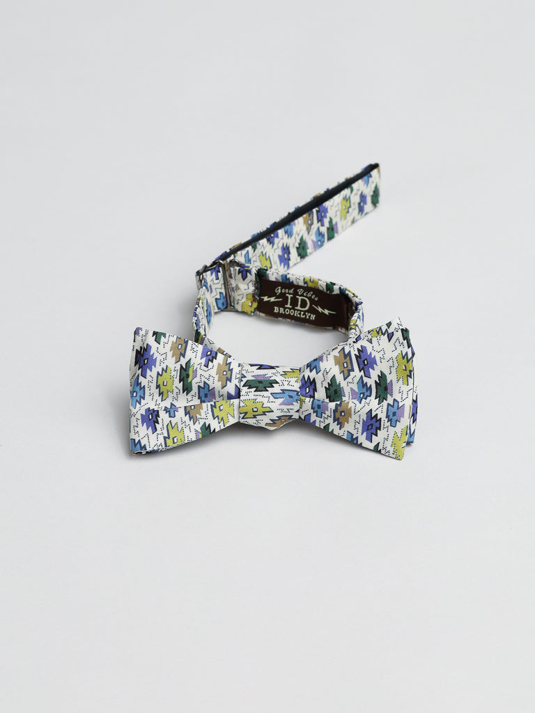 Handmade in Brooklyn, the ID Liberty of London Tana Lawn™ Sunrise Cotton Bowtie features a stylish geometric pattern in blue, green, and white. Created by ID Menswear, it adds flair to any dog collar. Set on a plain white background with the label reading H D Brooklyn.