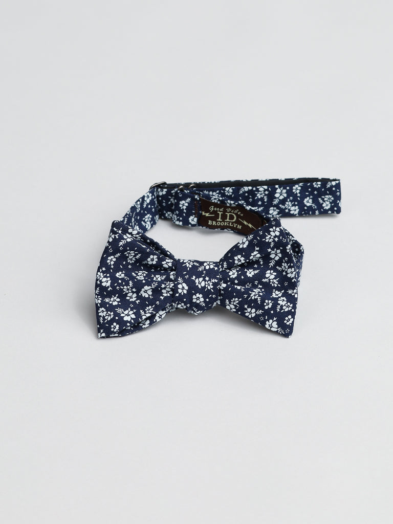 The Ditsy Cotton Bow Tie by ID Menswear is a navy blue, white floral pre-tied bow tie with an adjustable strap, handmade in Brooklyn. Shown on a plain background, its ideal for semi-formal looks.