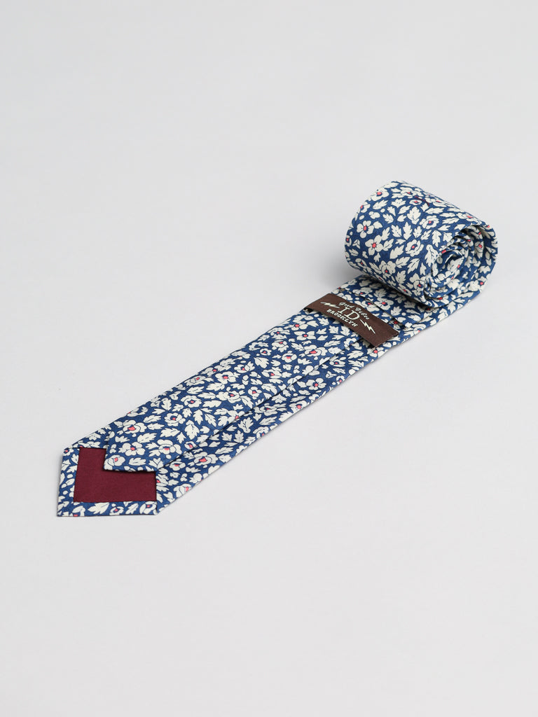 The Liberty of London Tana Lawn™ Feather Tie by ID Menswear, with a blue and white floral design and maroon tip, is crafted from fine cotton and photographed rolled on a plain light background.