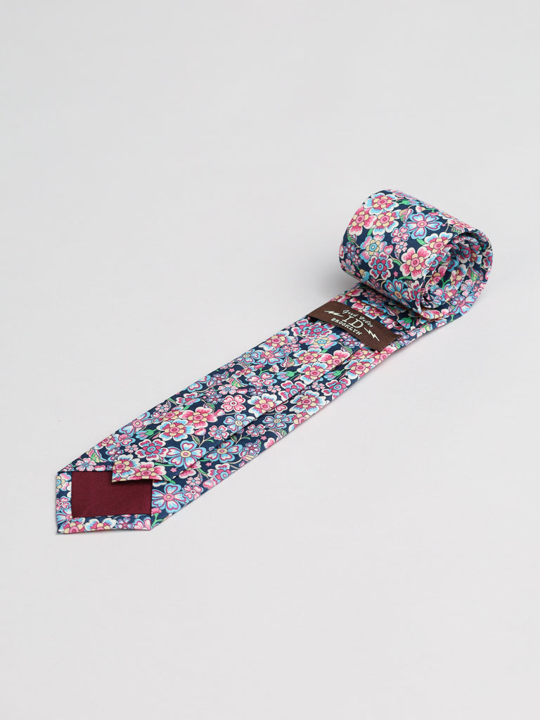 The ID Menswear Liberty of London Tana Lawn™ Anokhi Tie features a vibrant pink, blue, and white floral pattern on a dark background, is handmade in Brooklyn, and is shown rolled up on a white surface.