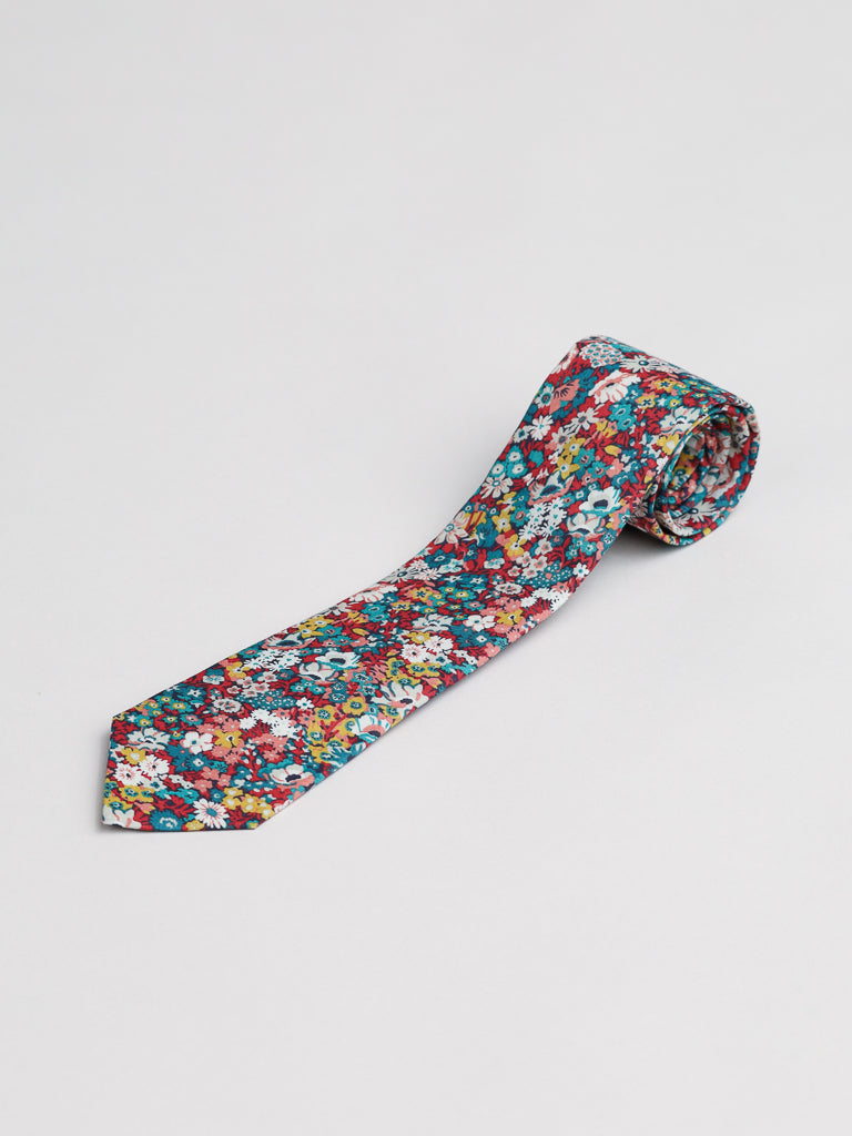 The Liberty of London Tana Lawn™ June Tie by ID Menswear features a handmade, rolled-up design with a vibrant floral print in red, blue, yellow, and white on a white background for a silk-like feel. Shown on a plain white surface.