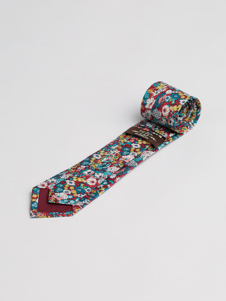 The Liberty of London Tana Lawn™ June Tie by ID Menswear is a handmade tie featuring a colorful floral pattern on white with red, blue, yellow, and green flowers, maroon lining at the tip, and a silk-like feel.