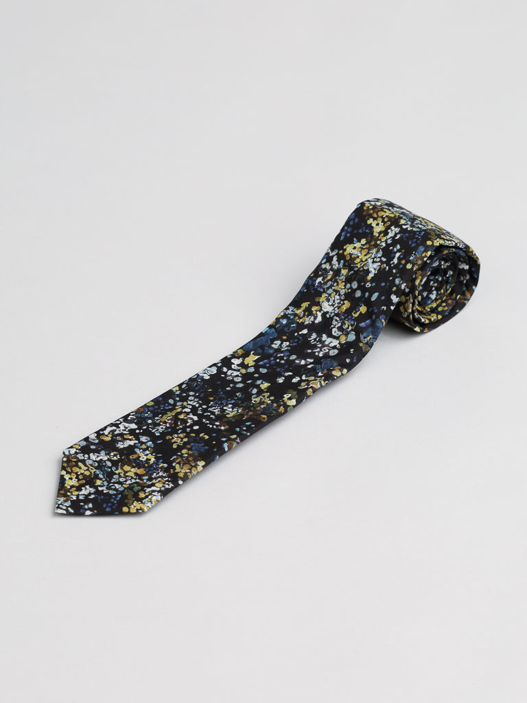 A rolled-up Liberty of London Tana Lawn™ Reflection Tie by ID Menswear, made from premium cotton and featuring a blue, yellow, and white floral pattern on a dark background, is displayed on a plain light surface.